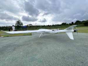 Side profile view of white long endurance hybrid VTOL fixed wing drone parked on outdoor test airfield ground, long range UAV for aerial mapping, land survey and infrastructure inspection