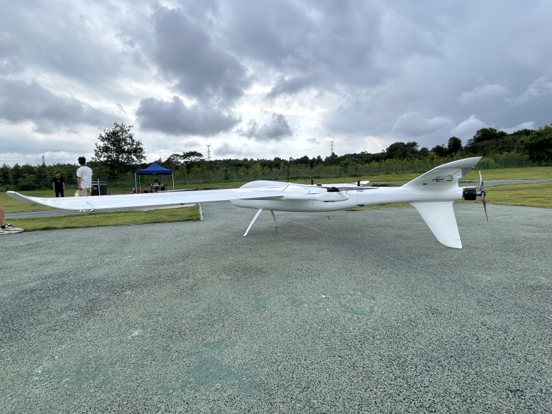 Side profile view of white long endurance hybrid VTOL fixed wing drone parked on outdoor test airfield ground, long range UAV for aerial mapping, land survey and infrastructure inspection