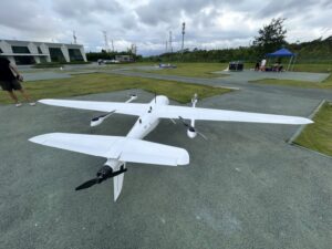 White hybrid VTOL fixed wing drone parked on the ground at outdoor test airfield, twin motor vertical takeoff landing UAV for aerial survey mapping and inspection missions