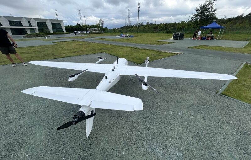 White hybrid VTOL fixed wing drone parked on the ground at outdoor test airfield, twin motor vertical takeoff landing UAV for aerial survey mapping and inspection missions
